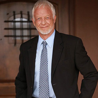 Photo of Dr. Elliott Maynard with white hair and beard wearing a suit